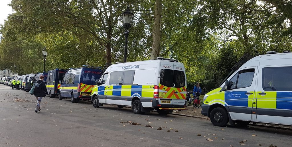 Line of police vans parked next to a park